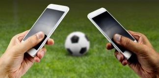 Two people hold phones while there is a football on the grass in front of them