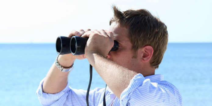 Man on beach looking through binoculars