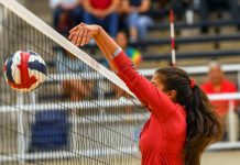 Female volleyball player spiking ball over net
