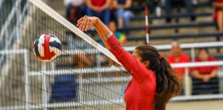 Female volleyball player spiking ball over net