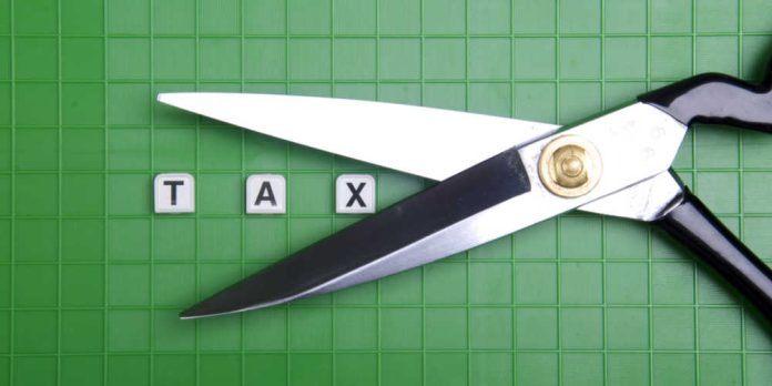 Scissors cutting around the word tax in block letters on a green background