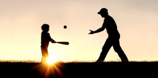 Silhouette of man throwing baseball to child with bat