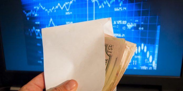 Money in envelope in front of stock trading screen
