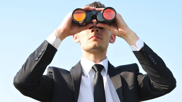 A man in a suit uses binoculars