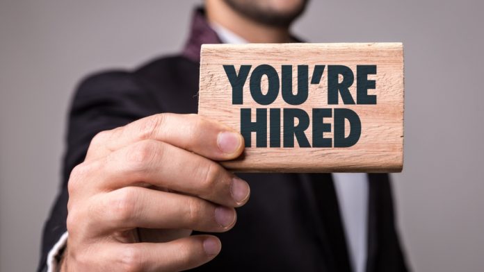 A man holds a sign saying You're Hired