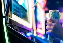A person grasping 50-dollar bills while sat at a slot machine