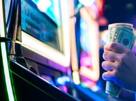 A person grasping 50-dollar bills while sat at a slot machine