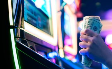 A person grasping 50-dollar bills while sat at a slot machine