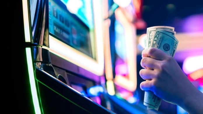 A person grasping 50-dollar bills while sat at a slot machine