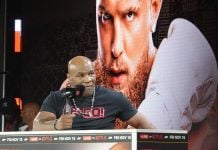 Mike Tyson speaking in front of a poster of Jake Paul