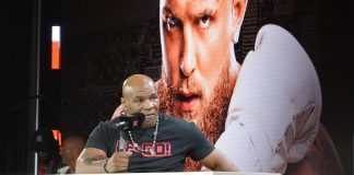 Mike Tyson speaking in front of a poster of Jake Paul