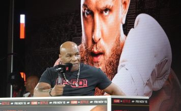 Mike Tyson speaking in front of a poster of Jake Paul