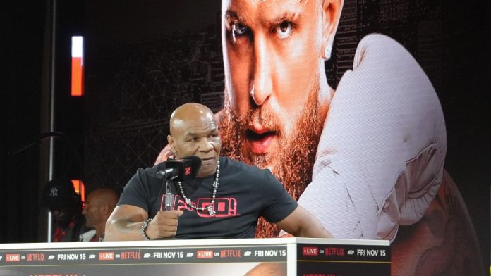 Mike Tyson speaking in front of a poster of Jake Paul