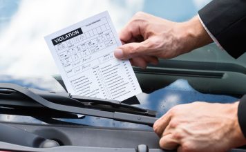 A person putting a violation notice on a car windshield