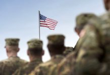 U.S. army personnel facing a flying American flag