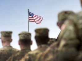 U.S. army personnel facing a flying American flag