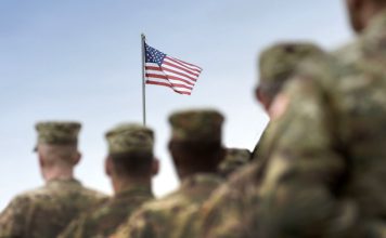 U.S. army personnel facing a flying American flag