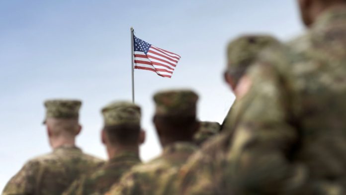 U.S. army personnel facing a flying American flag