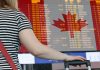 Woman looking at departures board at airport sporting Canadian flag