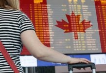 Woman looking at departures board at airport sporting Canadian flag