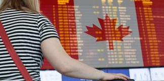 Woman looking at departures board at airport sporting Canadian flag