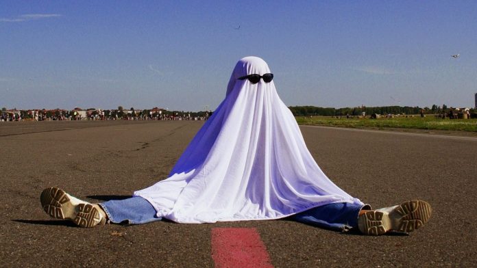 DraftKings-Summons-Ghost-Leg-Parlay-Feature-For-NFL-Season A person dressed as a ghost wearing sunglasses and sat with their legs spread