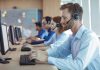 Several people sitting in line at a desk using phone headsets