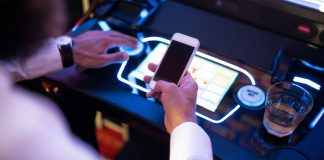 Man has phone at slot machine as Aristocrat acquires live slot streaming company Awager.