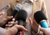 Several people holding up microphones to a person as if questioning them