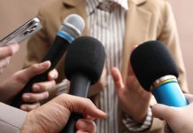 Several people holding up microphones to a person as if questioning them