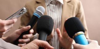 Several people holding up microphones to a person as if questioning them