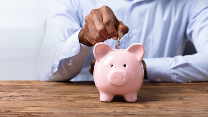 A person paying a coin into a piggy bank