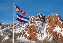The flags of the U.S. and Colorado flying in front of snowy brown mountains