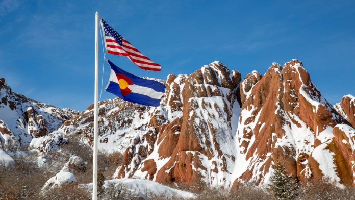 Colorado-fines-BetMGM-$50K-for-taking-$880-in-college-player-prop-bets The flags of the U.S. and Colorado flying in front of snowy brown mountains