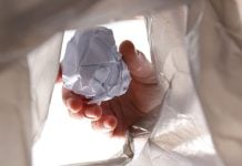 A person throwing crumpled up paper into a garbage bag