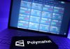 The Polymarket logo on a phone with trading markets on a laptop screen in the background