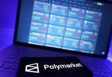 The Polymarket logo on a phone with trading markets on a laptop screen in the background