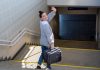 A woman waving goodbye over her shoulder as she heads to catch a subway train with a suitcase