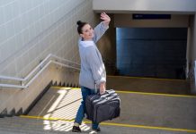 A woman waving goodbye over her shoulder as she heads to catch a subway train with a suitcase