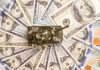 Toy tank sitting on a pile of hundred dollar bills