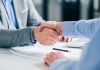 PENN extends retail sportsbook deal with Kambi Two businesspeople shaking hands with a pen and paper on the desk