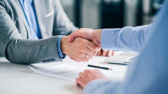 Two businesspeople shaking hands with a pen and paper on the desk