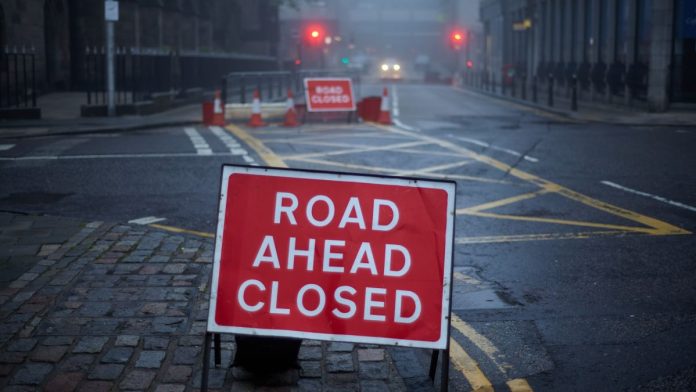 Roadworks on a deserted street with a sign stating "road ahead closed"