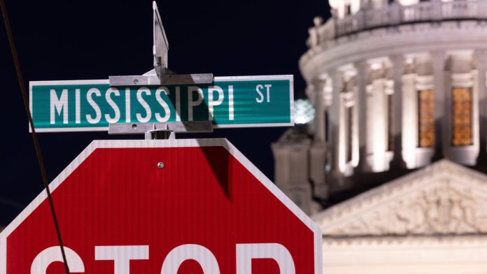 A road sign for Mississippi St. above a stop sign with the Mississippi State Capitol in the background