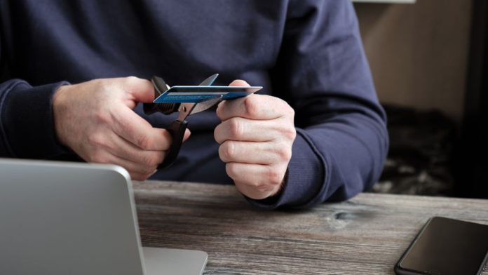 A person sat by a laptop cutting up a credit card