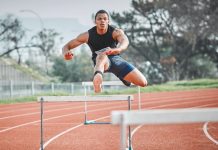 A male runner jumping hurdles on a track