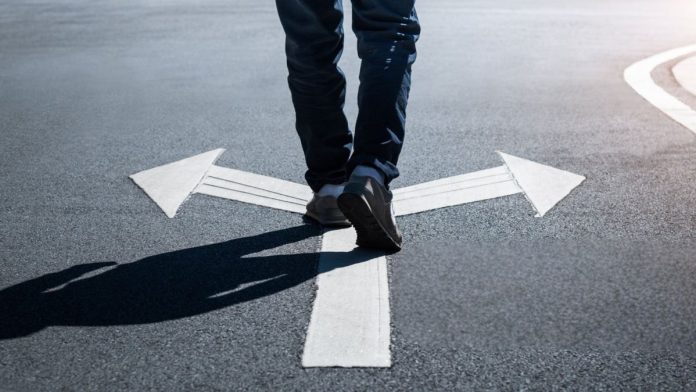A person walking on a road over arrows pointing in opposite directions